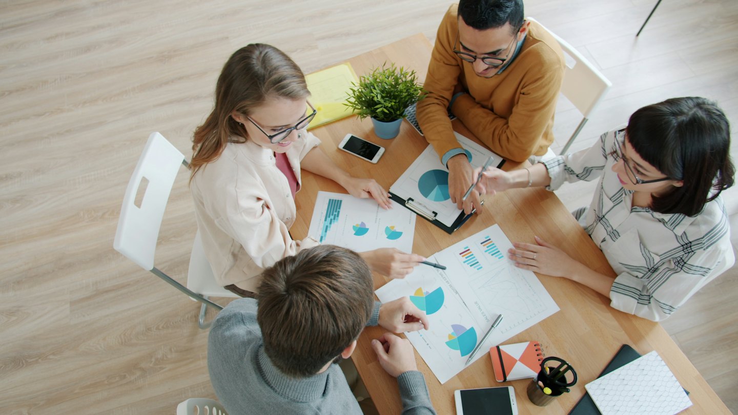 Diverse business team collaborates over financial charts at a table.