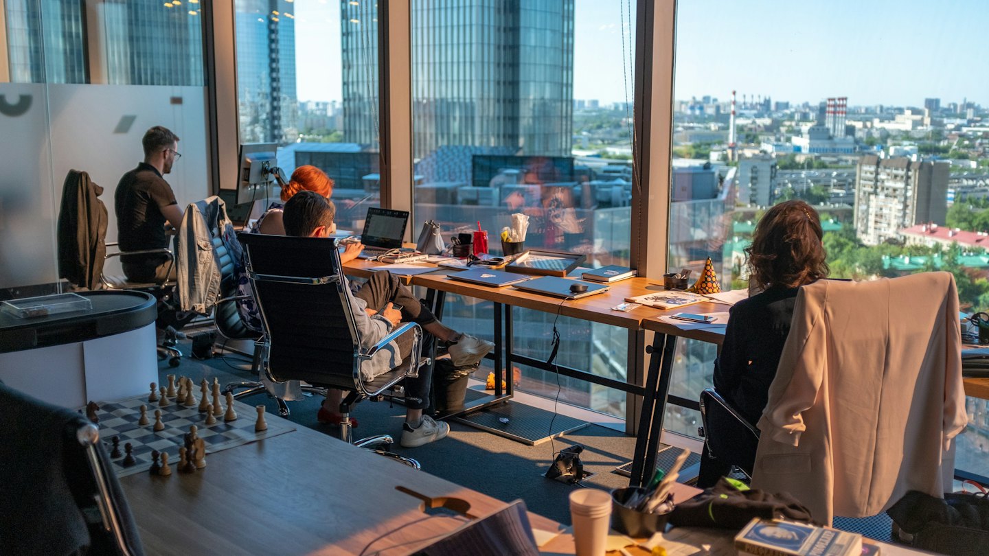 Professionals work at desks near large windows overlooking a city skyline.