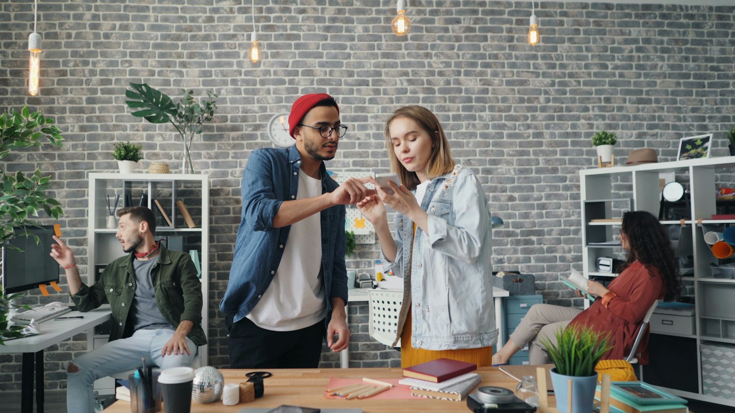 Colleagues collaborate on a smartphone in a bright, modern office.