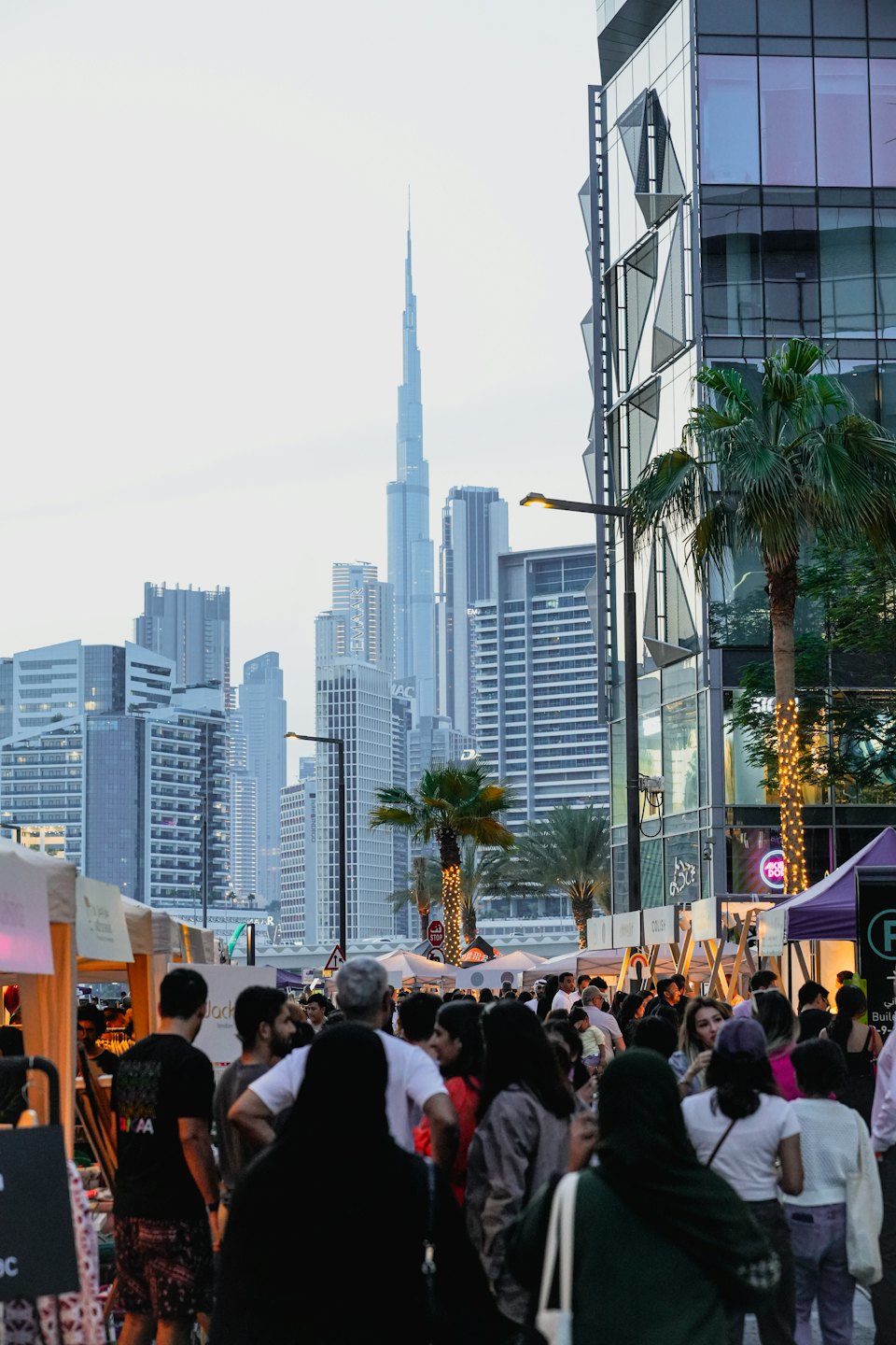 People walk through an outdoor market near tall city skyscrapers.